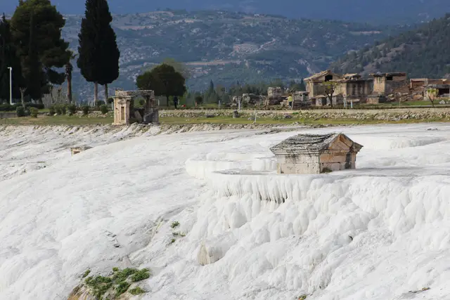 Beyaz travertenlerin üzerinde antik bir mezar ve arkada Hierapolis kalıntıları